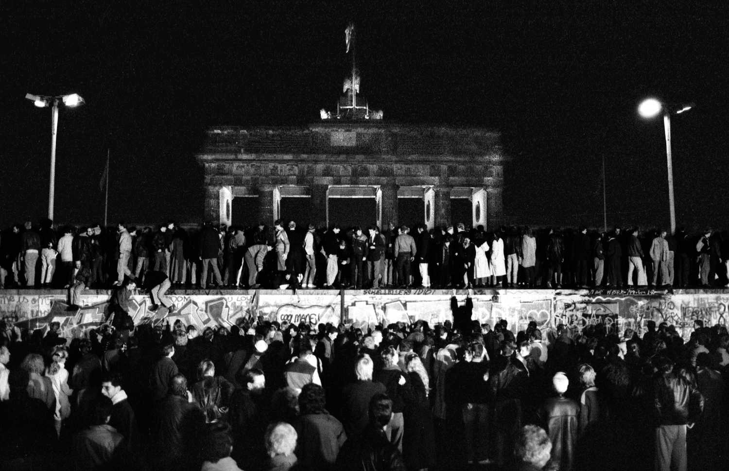 East and West German citizens celebrate as they climb the Berlin wall.