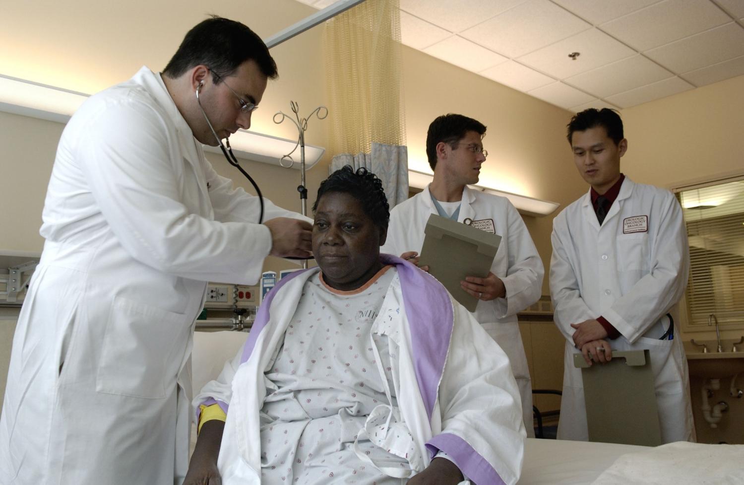 A doctor examines a patient, while other doctors look on