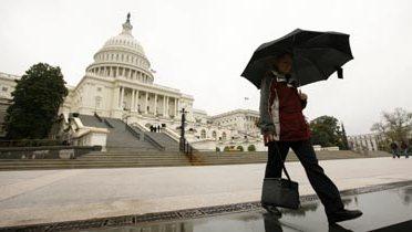 A person holding an umbrella walking near the U.S. Capitol building.