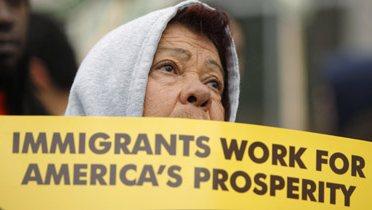 Woman holding sign reading "Immigrants work for America's prosperity"