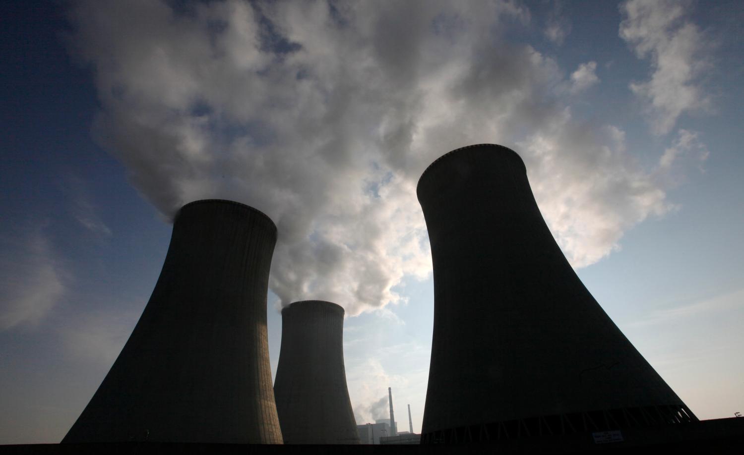 Three large smokestacks at a nuclear power plant stand against a cloudy sky.