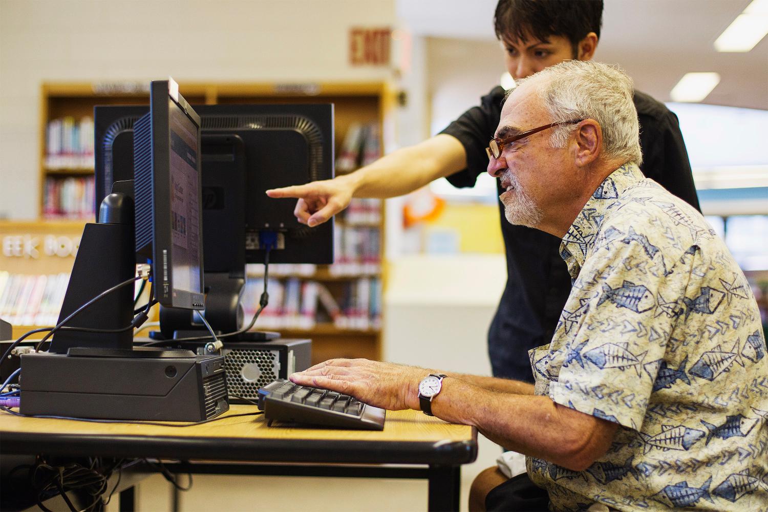 Child explains to a senior how to use a computer