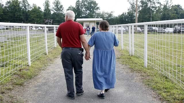 Two elderly individuals walk along a path in a rural area