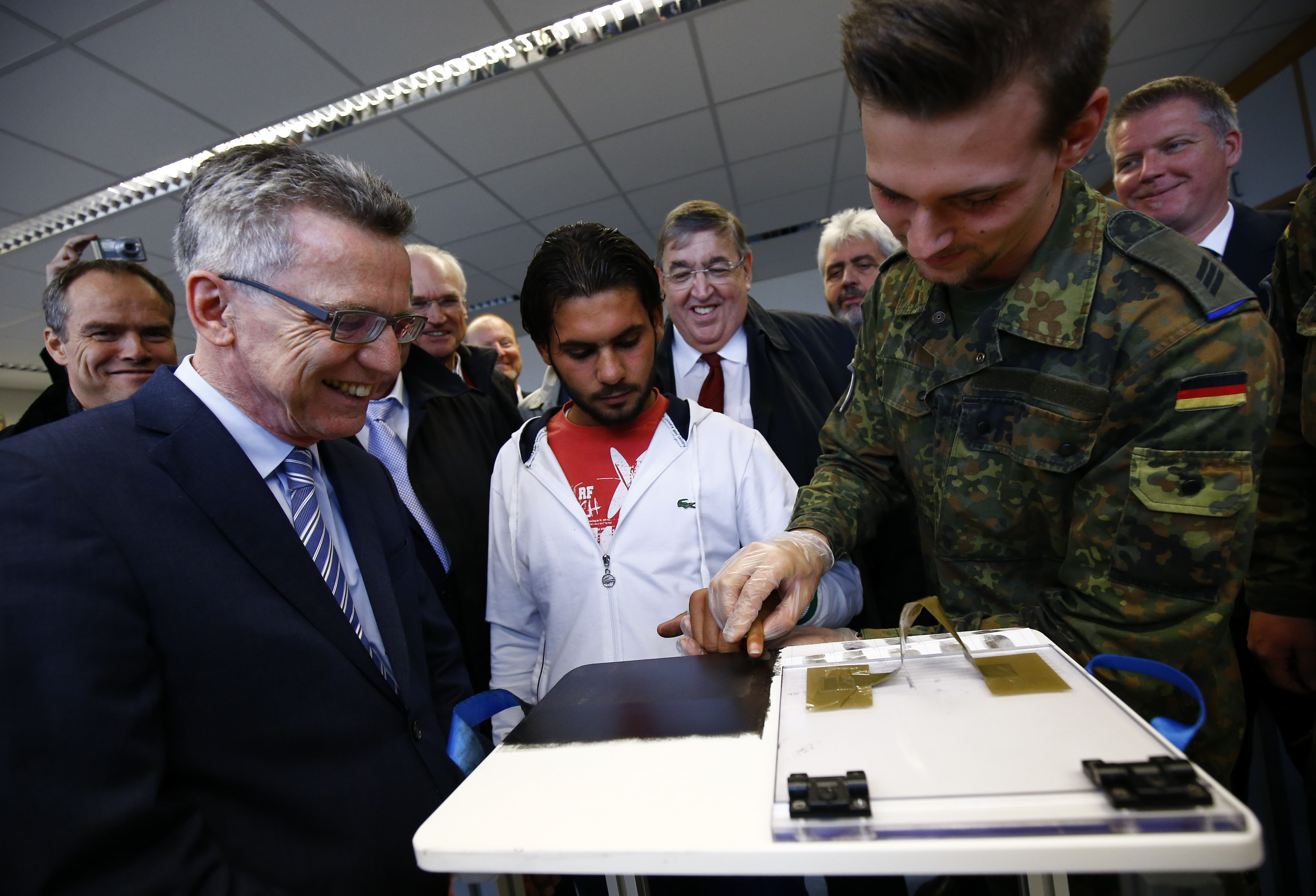 German Interior Minister Thomas de Maiziere (L) watches as a migrant from Babel in Iraq has his fingerprints taken, during a visit to Patrick-Henry Village refugee centre in Heidelberg, Germany October 22, 2015. Germany is introducing measures to tackle its refugee crisis earlier than previously expected, a top government official said on Friday, allowing accelerated deportation procedures to begin as early as next week. Germany expects a record influx of more than 800,000 migrants this year, by far the most in the European Union. With the new measures, Berlin is aiming to cope better with the unprecedented number of arrivals and to stem the influx. Picture taken October 22. REUTERS/Kai Pfaffenbach