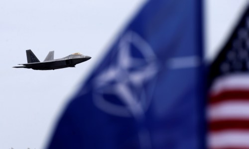 NATO and U.S. flags flutter as U.S. Air Force F-22 Raptor fighter flies over the military air base in Siauliai, Lithuania, April 27, 2016. REUTERS/Ints Kalnins