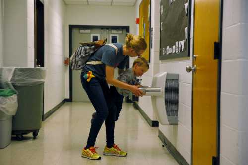 A woman helps her child get a drink from a fountain.