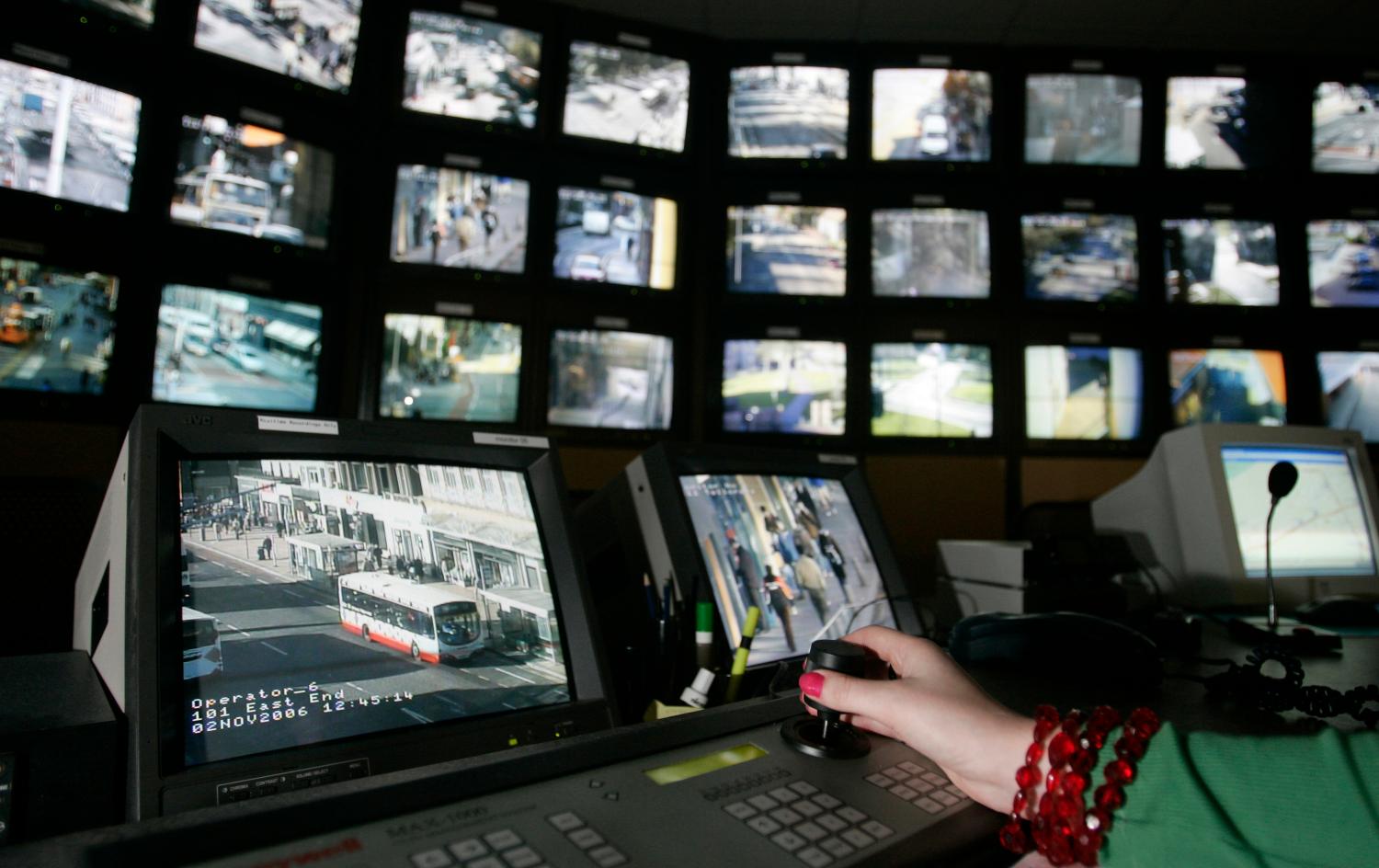 A surveillance monitoring expert uses a joystick to view a bank of screens