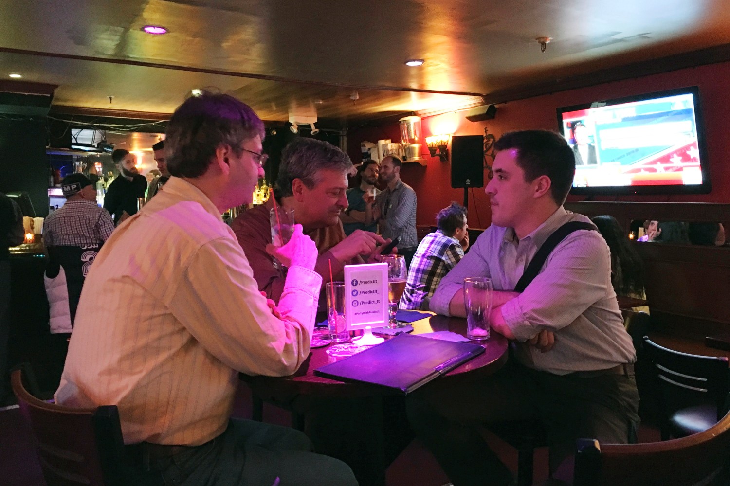 Three men, PredictIt traders, sit at a bar table in New York City awaiting presidential primary results.