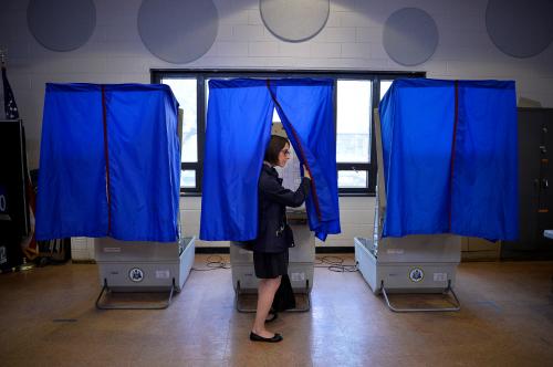 A voter leaves a voting booth, drawing back the privacy curtain.