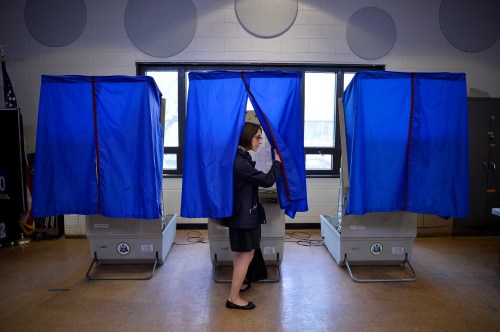 A voter leaves a voting booth, drawing back the privacy curtain.
