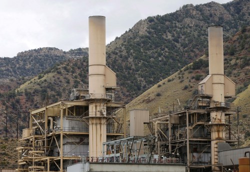 A large power plant in Colorado with two smoke stacks is seen with mountains rising in the background. No smoke is coming from the stacks.