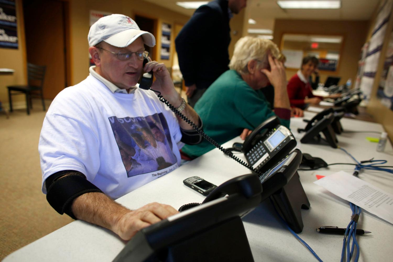 Seated at the end of a row of Romney/Ryan campaign volunteers, a man with three telephones in front of him speaks to a voter on one of them.