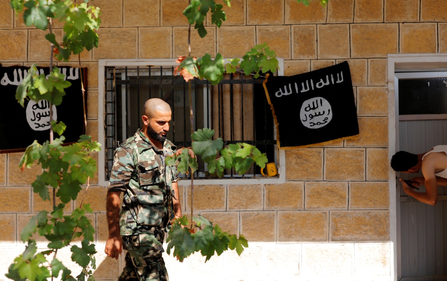 A member of Turkish-backed Free Syrian Army (FSA), seen with the Islamic State flags in the background, walks outside of a building in the border town of Jarablus, Syria, August 31, 2016. REUTERS/Umit Bektas - RTX2NQ7V