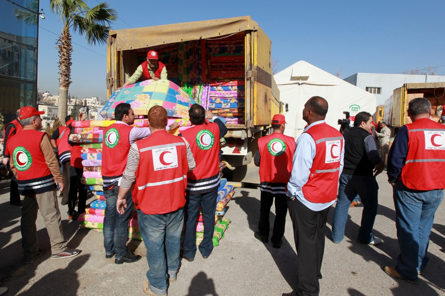 Iraqi and Jordanian Red Crescent workers load blankets and mattresses onto a truck, to deliver to Syrian refugees, in Amman February 10, 2013. About 3,000 Syrian refugee families living in Jordan received humanitarian aid from the Iraqi Red Crescent organization, in coordination with the Jordanian Red Crescent, the organisation said. REUTERS/Muhammad Hamed (JORDAN - Tags: POLITICS SOCIETY IMMIGRATION) - RTR3DKK1