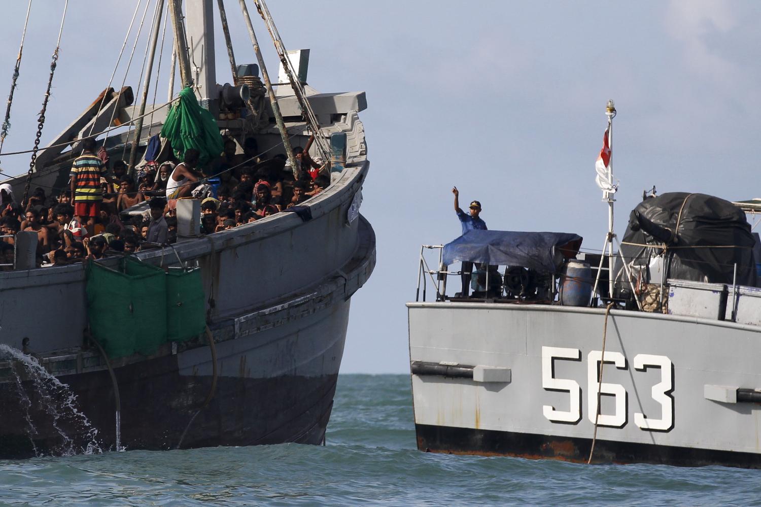 A Myanmar military officer (R) gestures from a navy ship towards a boat packed with migrants, off Leik Island in the Andaman Sea May 31, 2015. More than 700 migrants found packed aboard an overcrowded boat in the Andaman Sea were still being held offshore by Myanmar's navy on Monday, more than three days after the converted fishing vessel was intercepted off the country's coast. Picture taken May 31, 2015. REUTERS/Soe Zeya Tun - RTR4YF8E