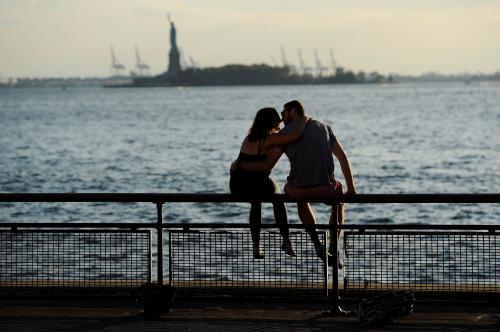 A couple kiss as they watch the sunset silhouette the Statue of Liberty from Battery Park in New York