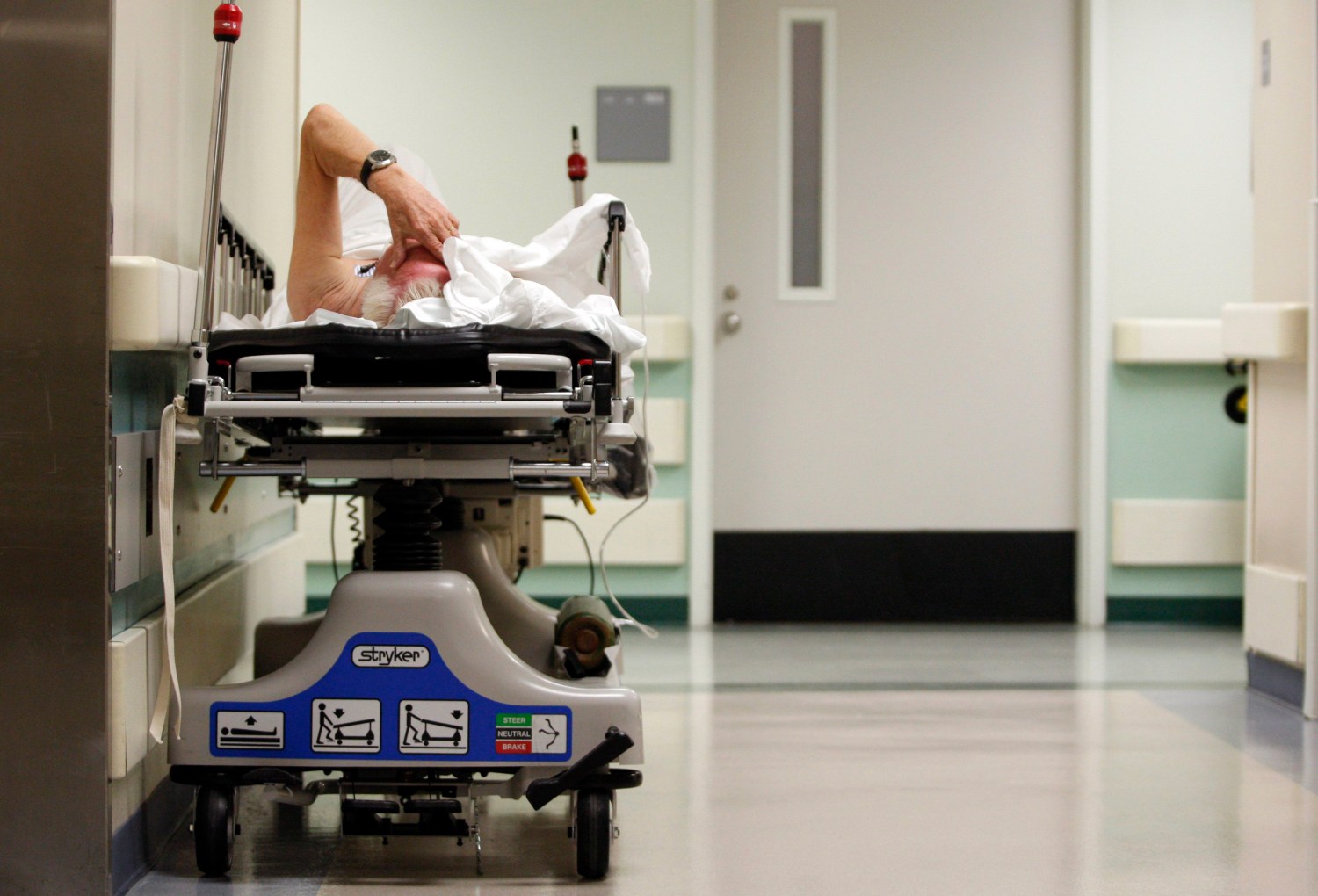A patient lies in a hospital bed in a hospital hallway