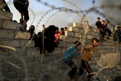 Newly displaced people run after they jumped over a wall to get humanitarian packages, as a smoke rises from a burning oil refinery, at a processing center in Qayyara, south of Mosul, Iraq October 25, 2016. REUTERS/Zohra Bensemra - RTX2QDKI