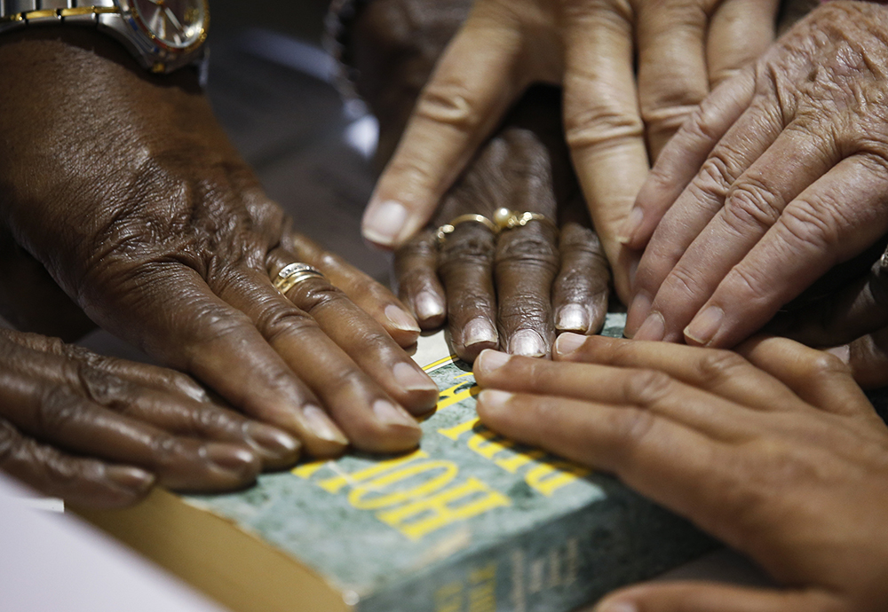 Hands of poll workers are seen on a Bible as head precinct judge Deloris Reid-Smith reads the voters oath to poll workers before opening the polls