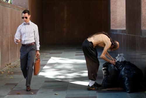 A man looks at his phone as he walks out of courthouse past man arranging bags in Los Angeles