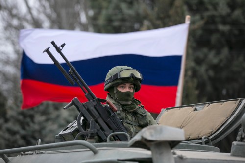 A Russian soldier in front of a flag.