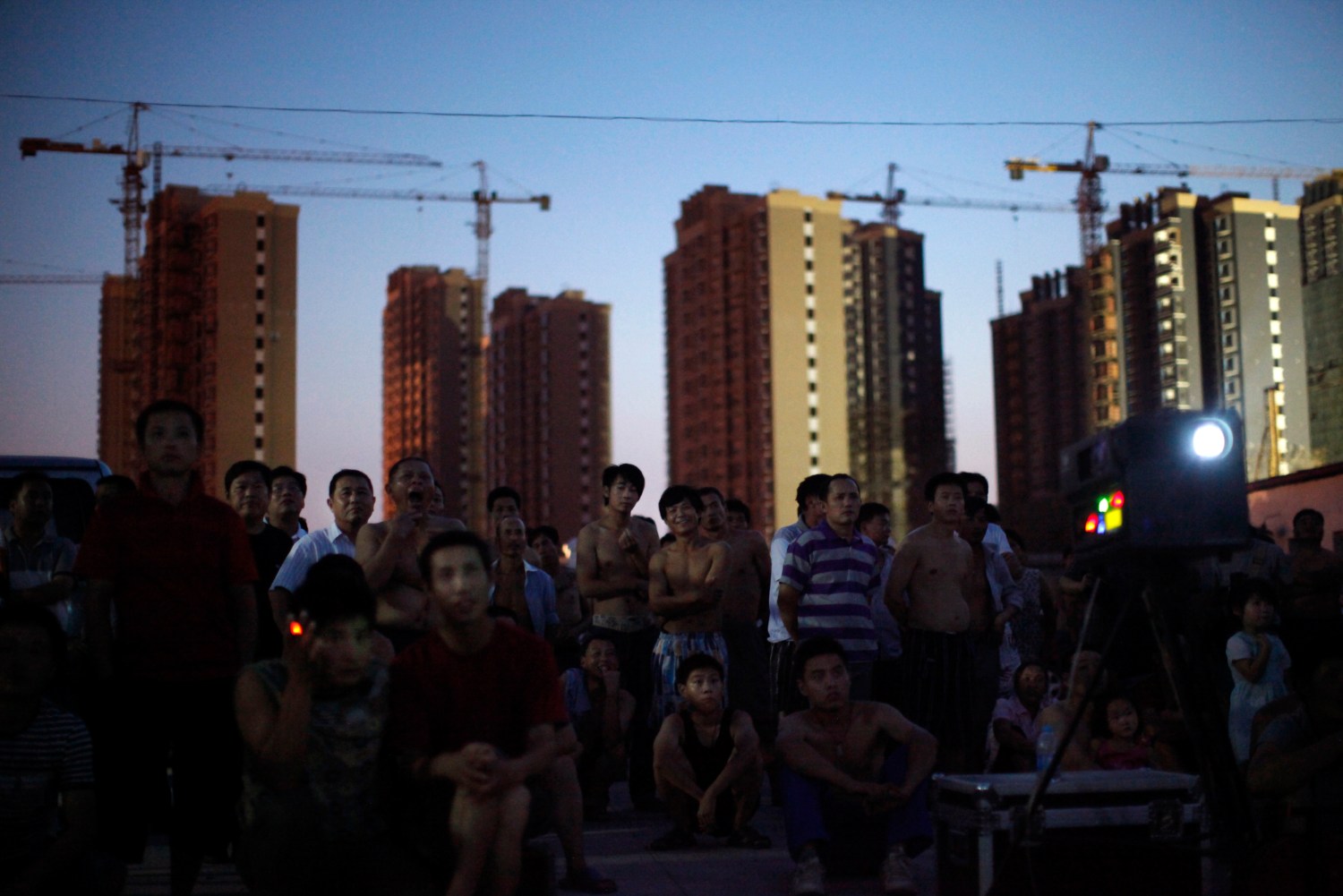 Migrant construction workers watch an open air movie near their dormitories after a shift at a residential construction site in Shanghai July 15, 2013. The construction site is among a new developing residential area located in Jiading district of suburban Shanghai, some 30 kilometres from the city centre. According to data from the World Bank, 68 percent of China's female population aged 15 and above participate in the labour force, compared to 58 percent in the United States, 51 percent in France, and 53 percent in Germany. Around a third of China's millions of rural-urban migrant workers are women and according to an academic paper published 2010, they also earn around a third less than their male equivalents. Picture taken July 15, 2013. REUTERS/Aly Song (CHINA - Tags: BUSINESS EMPLOYMENT SOCIETY CONSTRUCTION) ATTENTION EDITORS: PICTURE 28 OF 29 FOR PACKAGE 'CHINA'S MIGRANT WORKFORCE'. TO FIND ALL IMAGES SEARCH 'RURAL-URBAN SONG' - RTX13N5Z