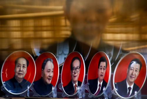 A woman is reflected in a shop window as she looks at souvenir plates with portraits of former Chinese leaders Mao Zedong, Deng Xiaoping, Jiang Zemin, Hu Jintao and current President Xi Jinping
