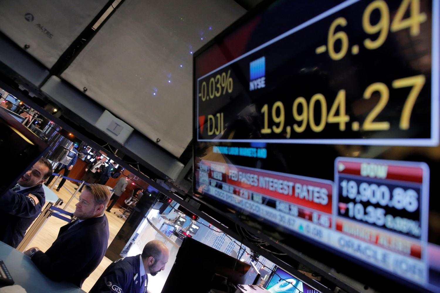 Traders work on the floor of the New York Stock Exchange (NYSE) as a television screen shows news of the announcement that the U.S. Federal Reserve will hike interest rates.