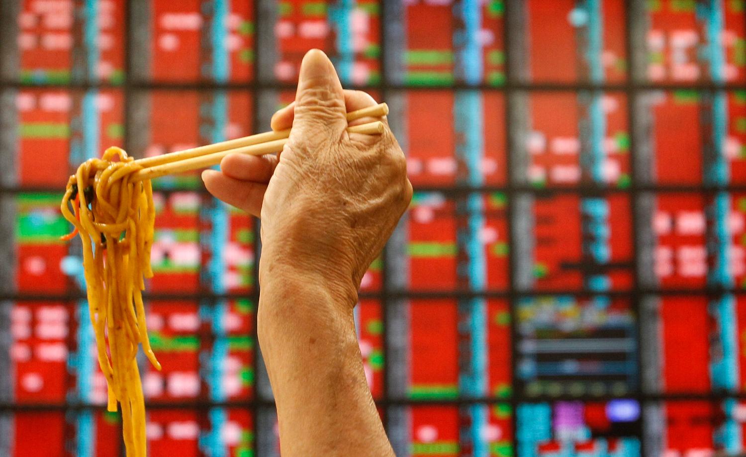 A man eats his lunch of noodles while monitoring stock market prices inside a brokerage in Taipei August 10, 2011.