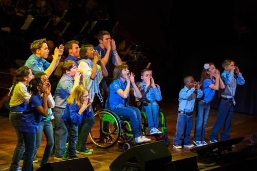 Children who have attended one of several camps for disabled children perform on stage