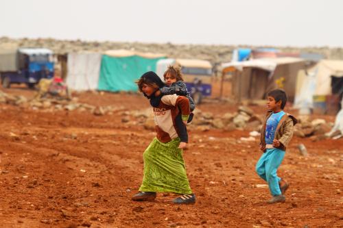 An Internally displaced Syrian youth carries a baby on her back inside a refugee camp in the Hama countryside, Syria January 1, 2016. REUTERS/Ammar Abdullah - RTX20QUV