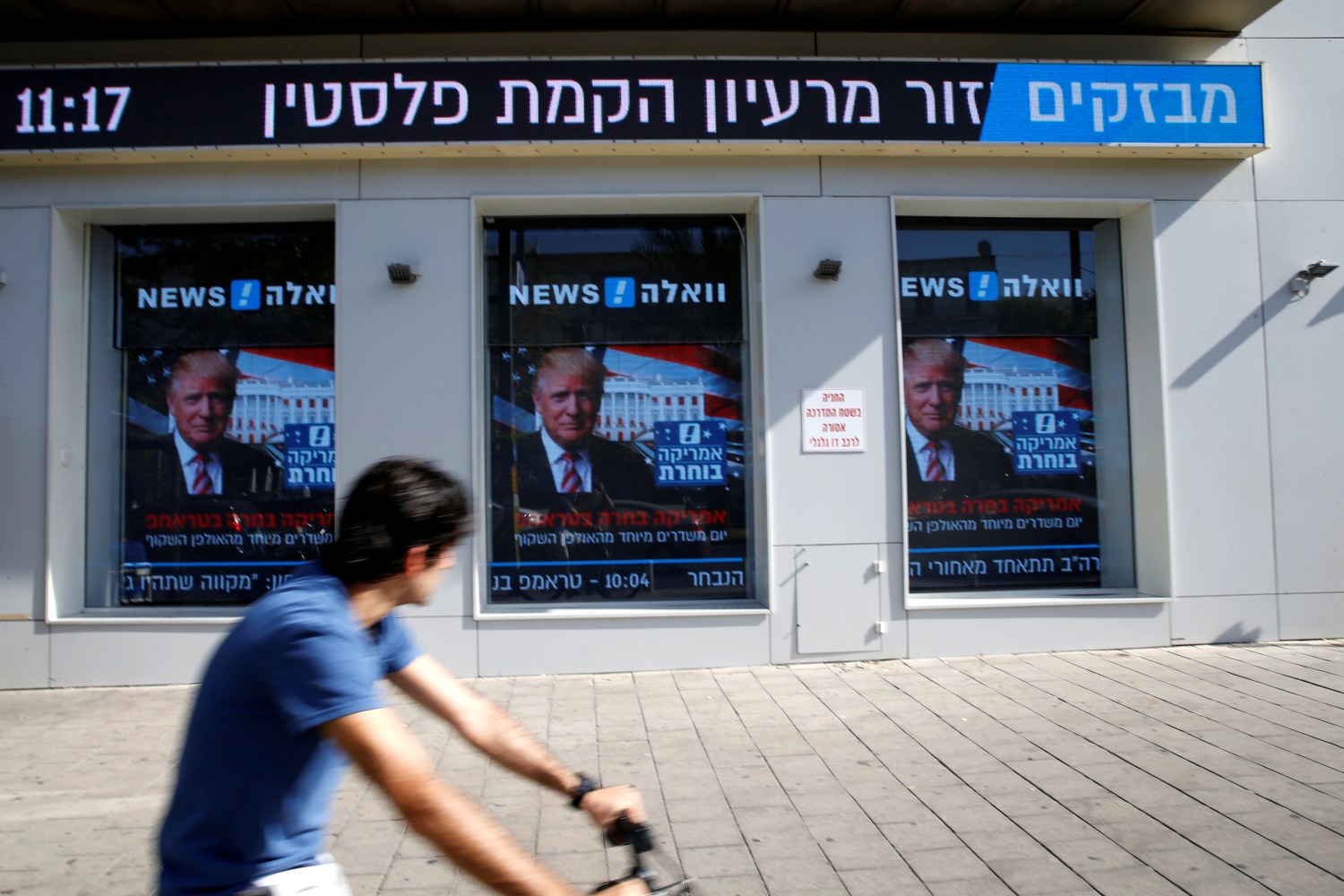 A man cycles past images of newly elected U.S. President Donald Trump which are displayed on monitors in Tel Aviv, Israel November 9, 2016. REUTERS/Baz Ratner - RTX2SSC2