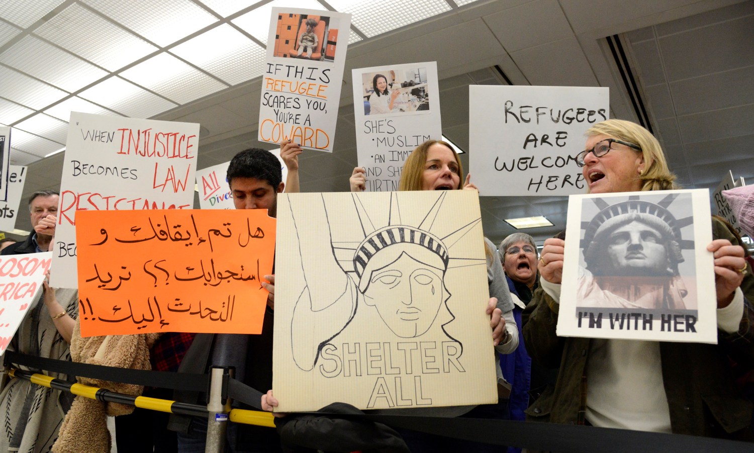 Dozens of pro-immigration demonstrators cheer and hold signs as international passengers arrive at Dulles International Airport, to protest President Donald Trump's executive order barring visitors, refugees and immigrants from certain countries to the United States, in Chantilly, Virginia, in suburban Washington, U.S., January 29, 2017. The sign in Arabic (L) reads "Have you been stopped and questioned, we would like to talk to you, to assist with a lawyer". REUTERS/Mike Theiler - RTSXYQ0