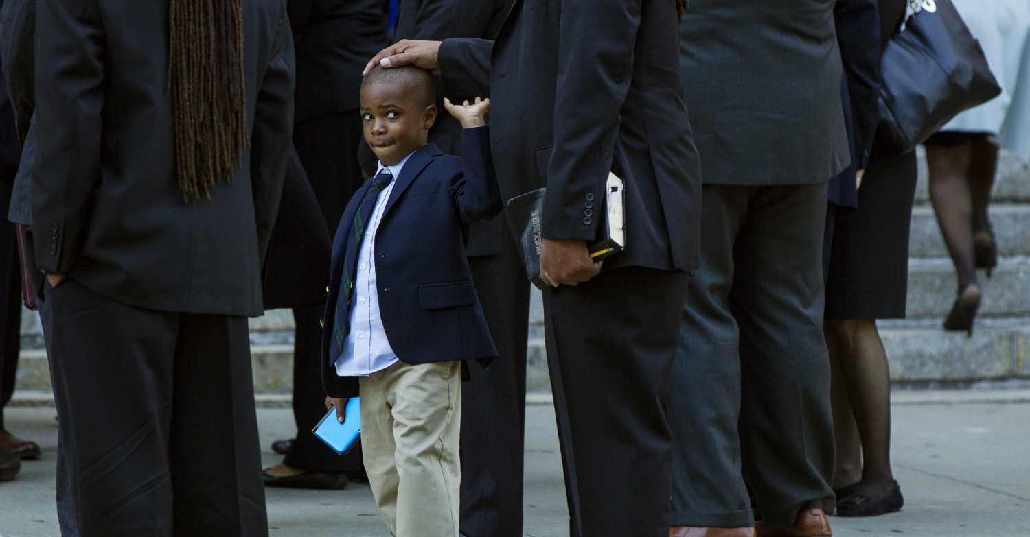 A young boy reaches to remove his father's hand from his head.