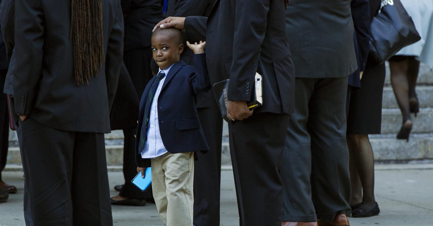 A young boy reaches to remove his father's hand from his head.