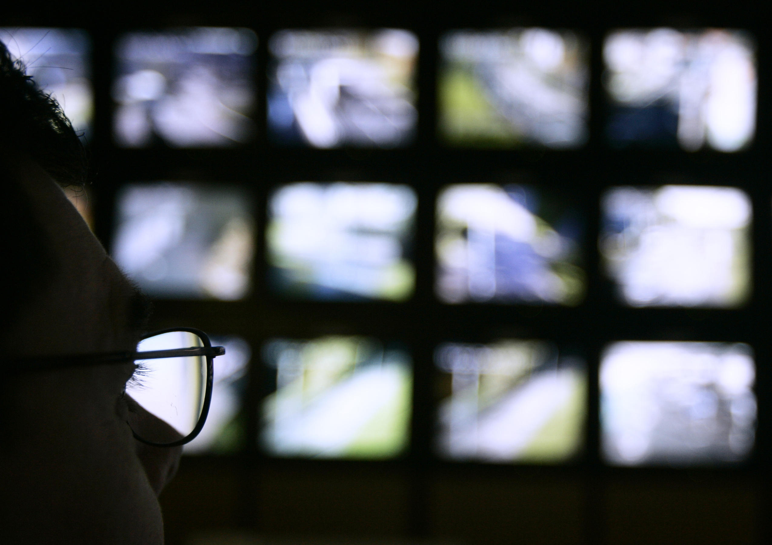 A surveillance monitoring expert watches a bank of screens showing images