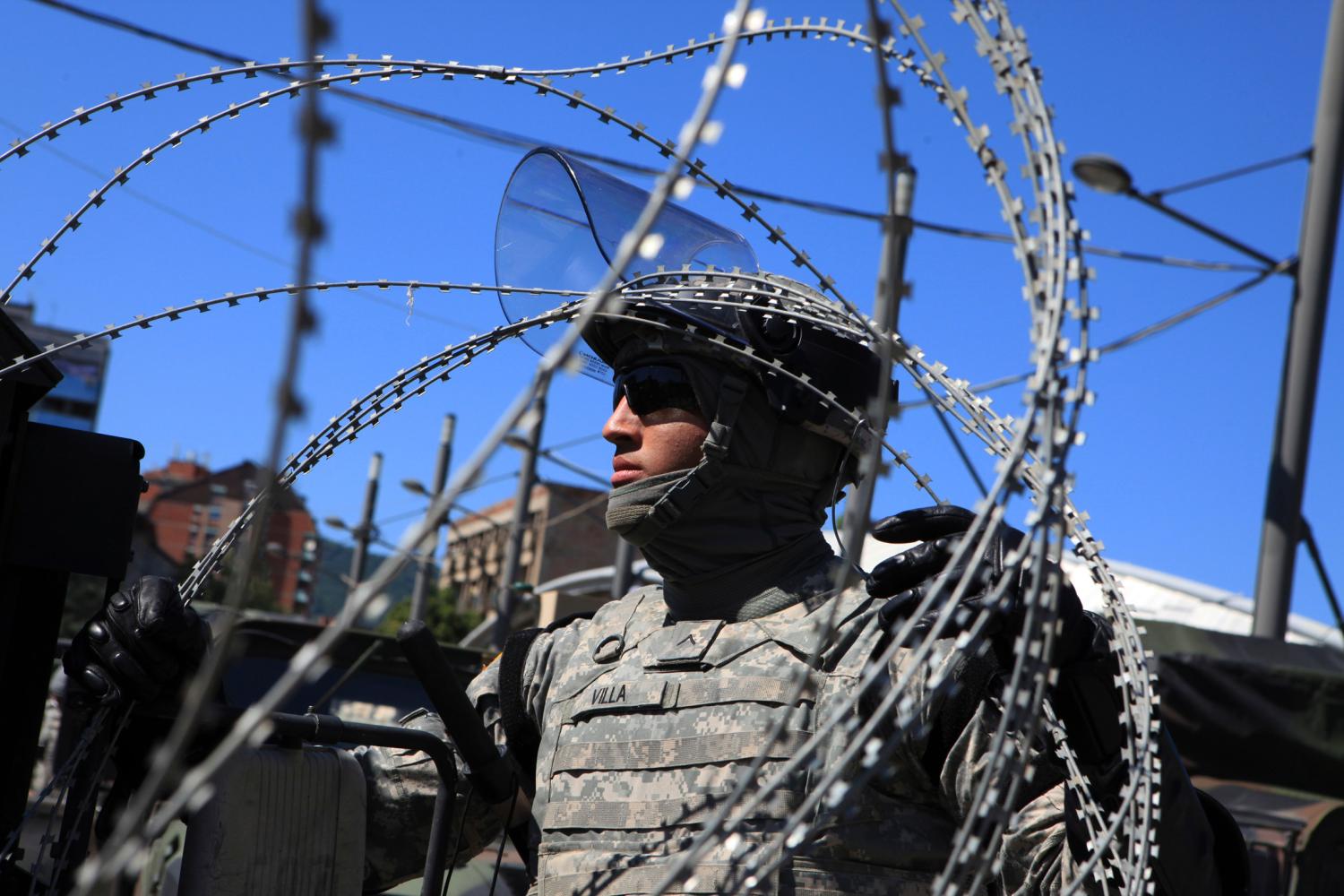 A U.S. soldier, part of a NATO peace force, places barbed wire on his Humvee during a protest in the ethnically divided town of Mitrovica June 22, 2014. Police in Kosovo fired tear gas and rubber bullets on Sunday at ethnic Albanian rioters burning police cars and lobbing rocks in Mitrovica, in protest over the blockage of the main bridge by ethnic Serbs. REUTERS/Hazir Reka (KOSOVO - Tags: POLITICS MILITARY CIVIL UNREST) - RTR3V4GC