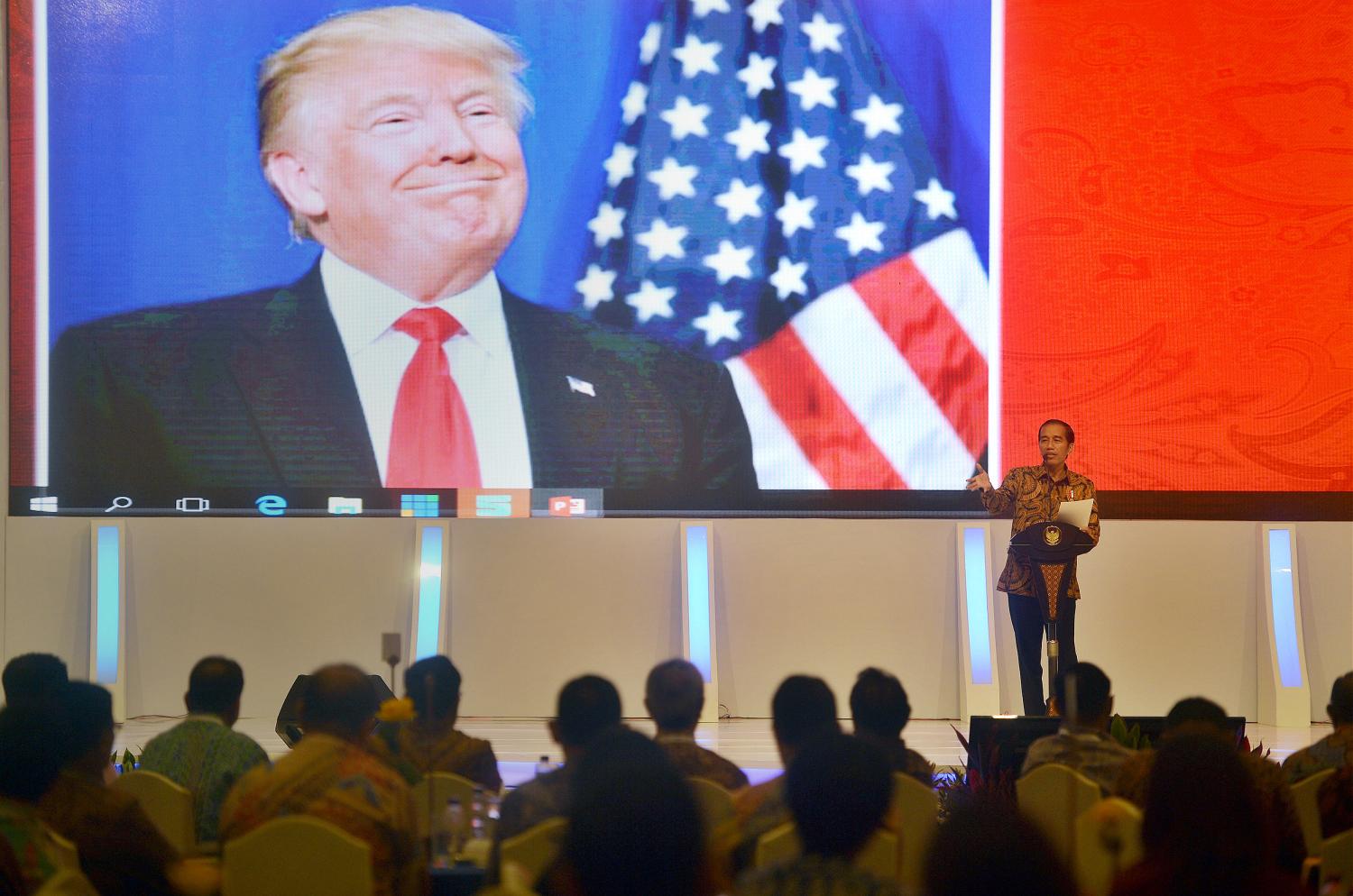 Indonesian President Joko Widodo speaks to local company executives as a picture of U.S. President-elect Donald Trump is shown on a screen behind him