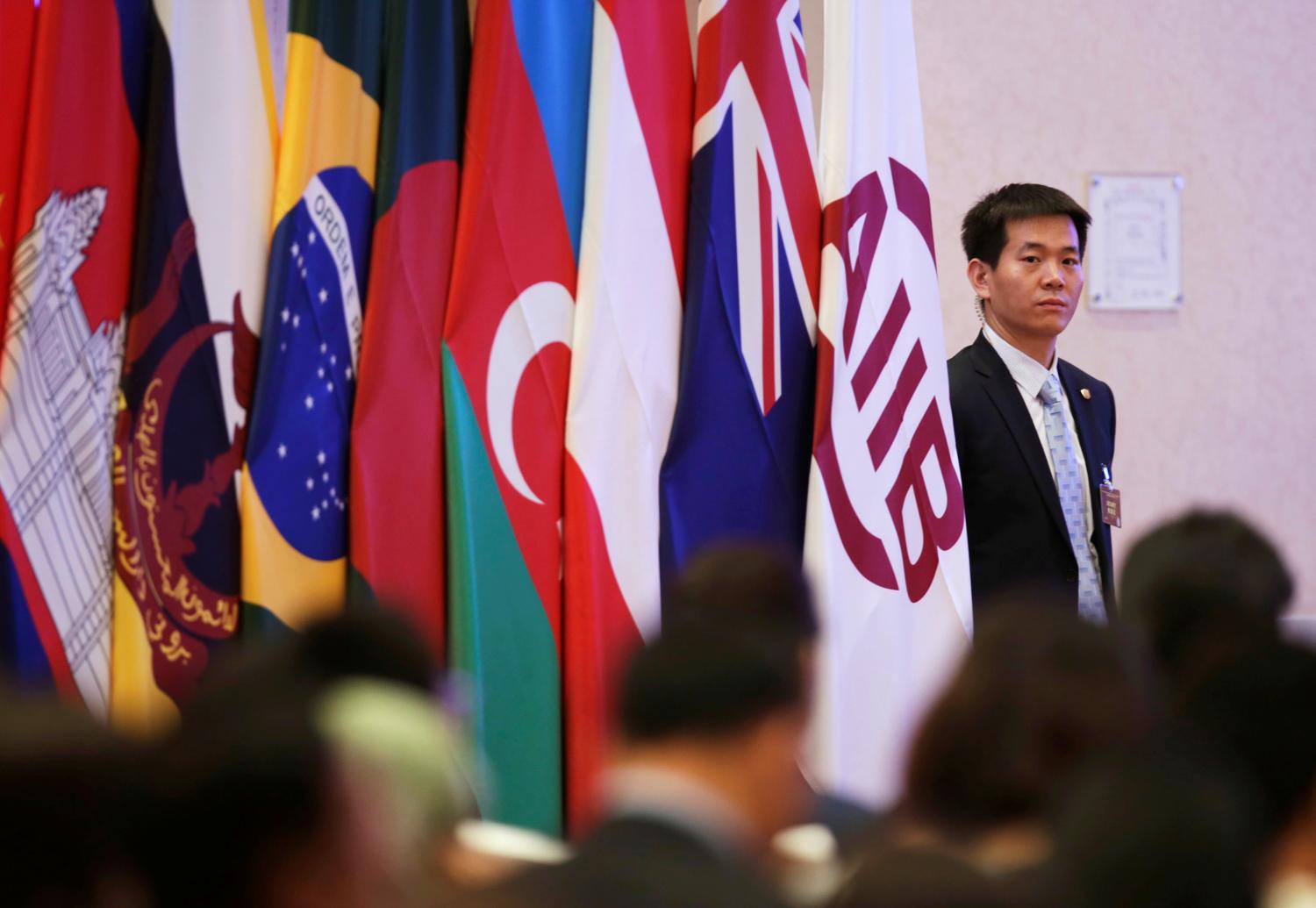 A security personnel stands next to an Asian Infrastructure Investment Bank (AIIB) flag during the opening ceremony of the first annual meeting of AIIB in Beijing, China, June 25, 2016.