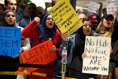 Dozens of pro-immigration demonstrators cheer and hold signs as international passengers arrive at Dulles International Airport in Chantilly, Virginia