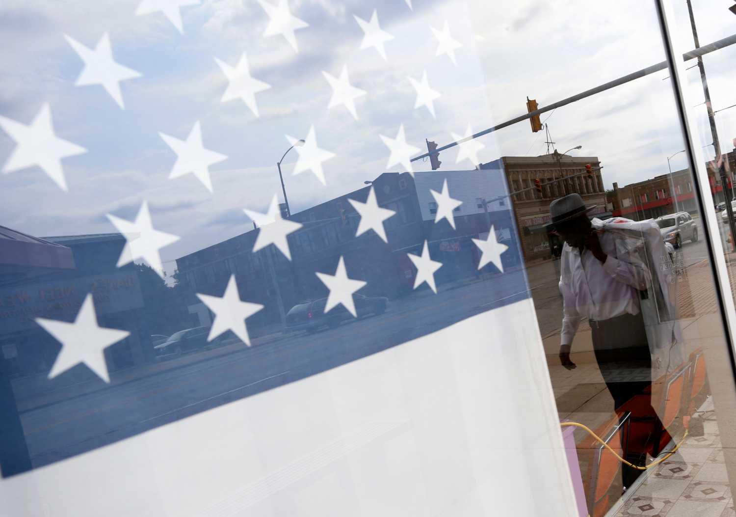 A man is reflected in a storefront window as he walks along a street.