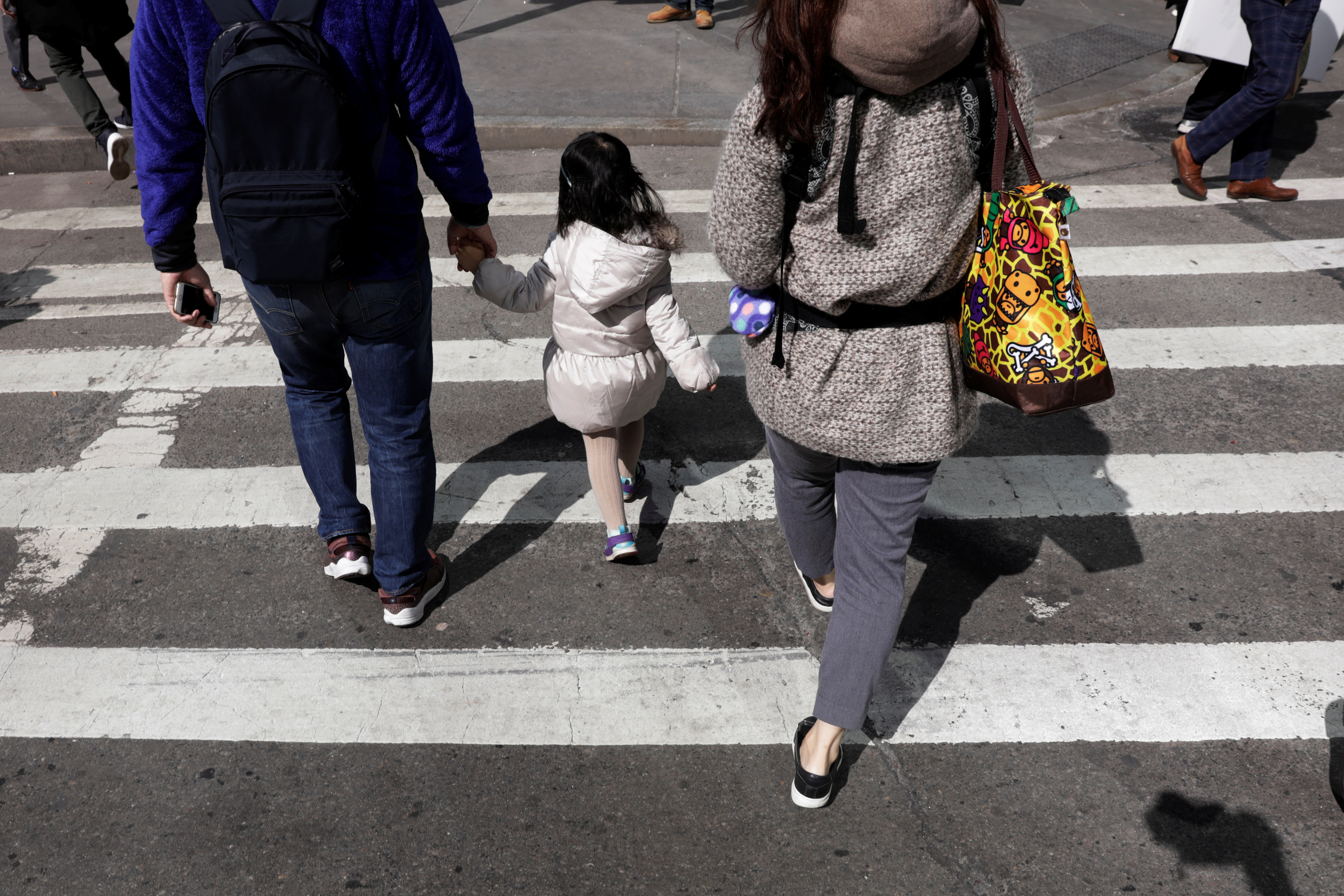 A family holds hands as they cross the street on the first day of Spring in New York.