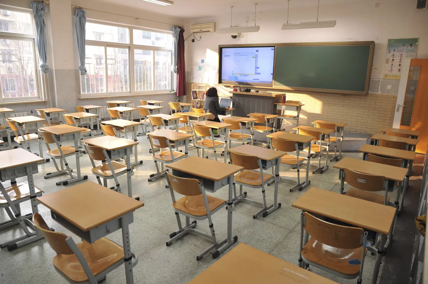 A Chinese language teacher sits in an empty classroom as she teaches a class during an online course at Jingshan School, on a smoggy day under a "red alert" for air pollution, in Beijing