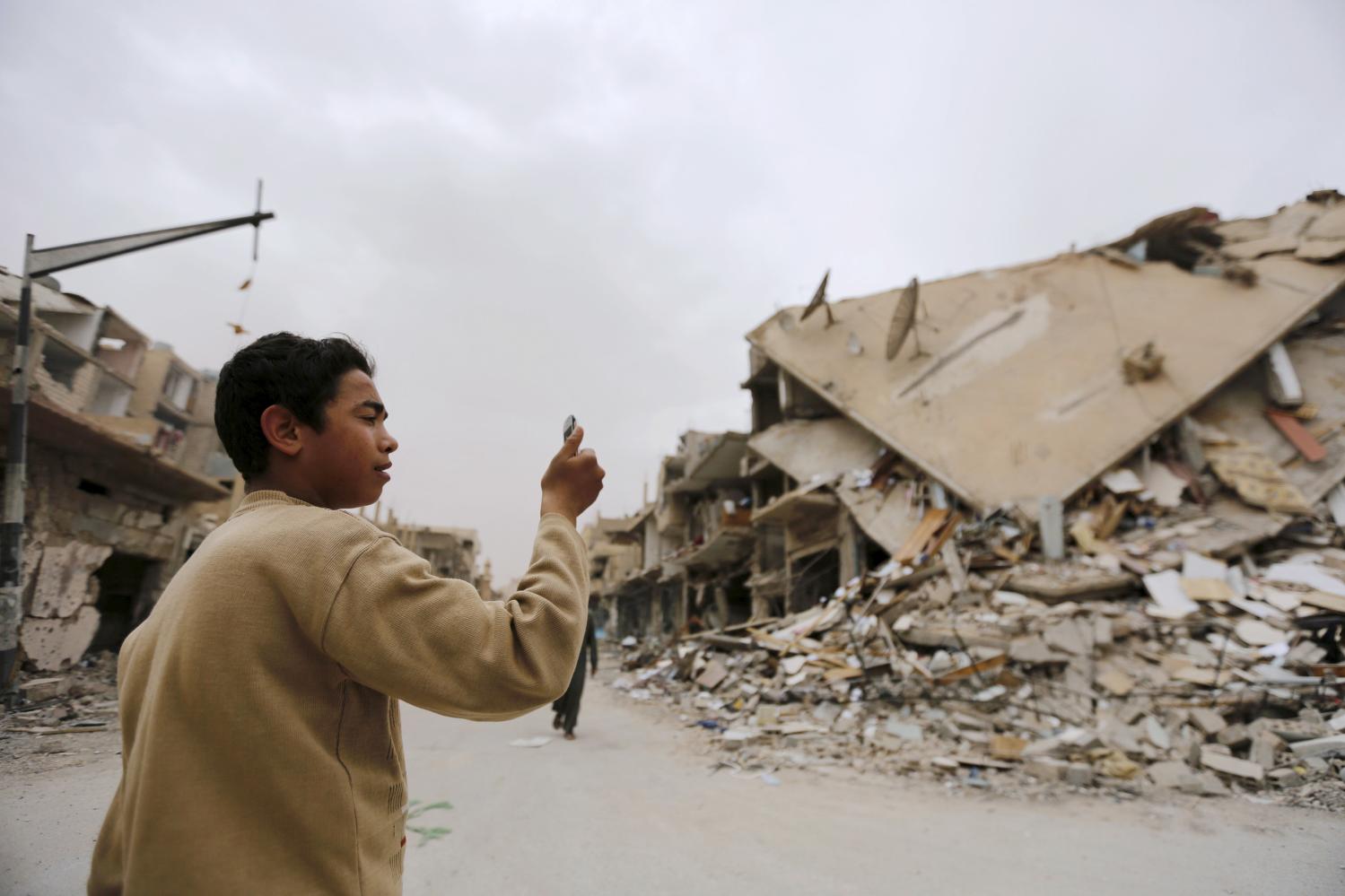 A boy takes a picture with his mobile phone of damaged buildings during his visit to the city of Palmyra, Syria