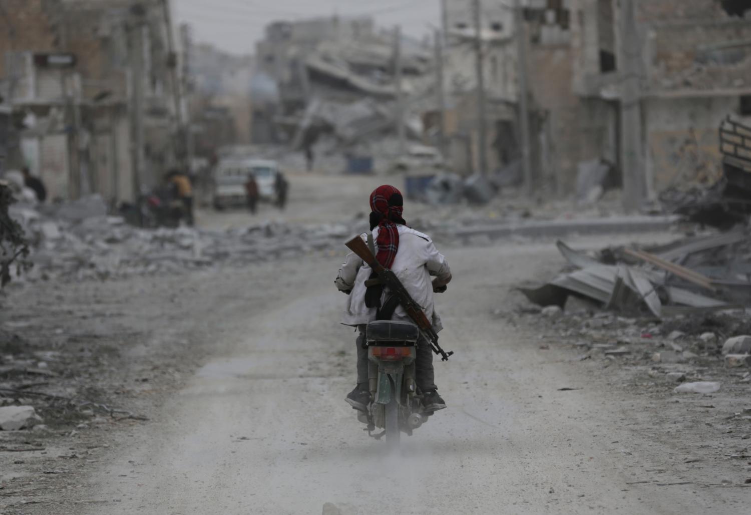 A man drives a motorcycle while carrying his weapon near damaged buildings in the northern Syrian town of al-Bab, Syria March 1, 2017. REUTERS/Khalil Ashawi - RTS111JX