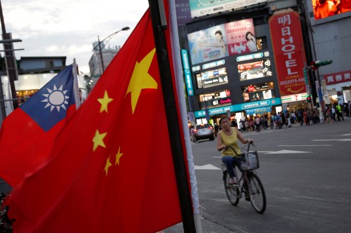 A woman rides a bike past Taiwan and China national flags during a rally held by a group of pro-China supporters calling peaceful reunification, 6 days before the inauguration ceremony