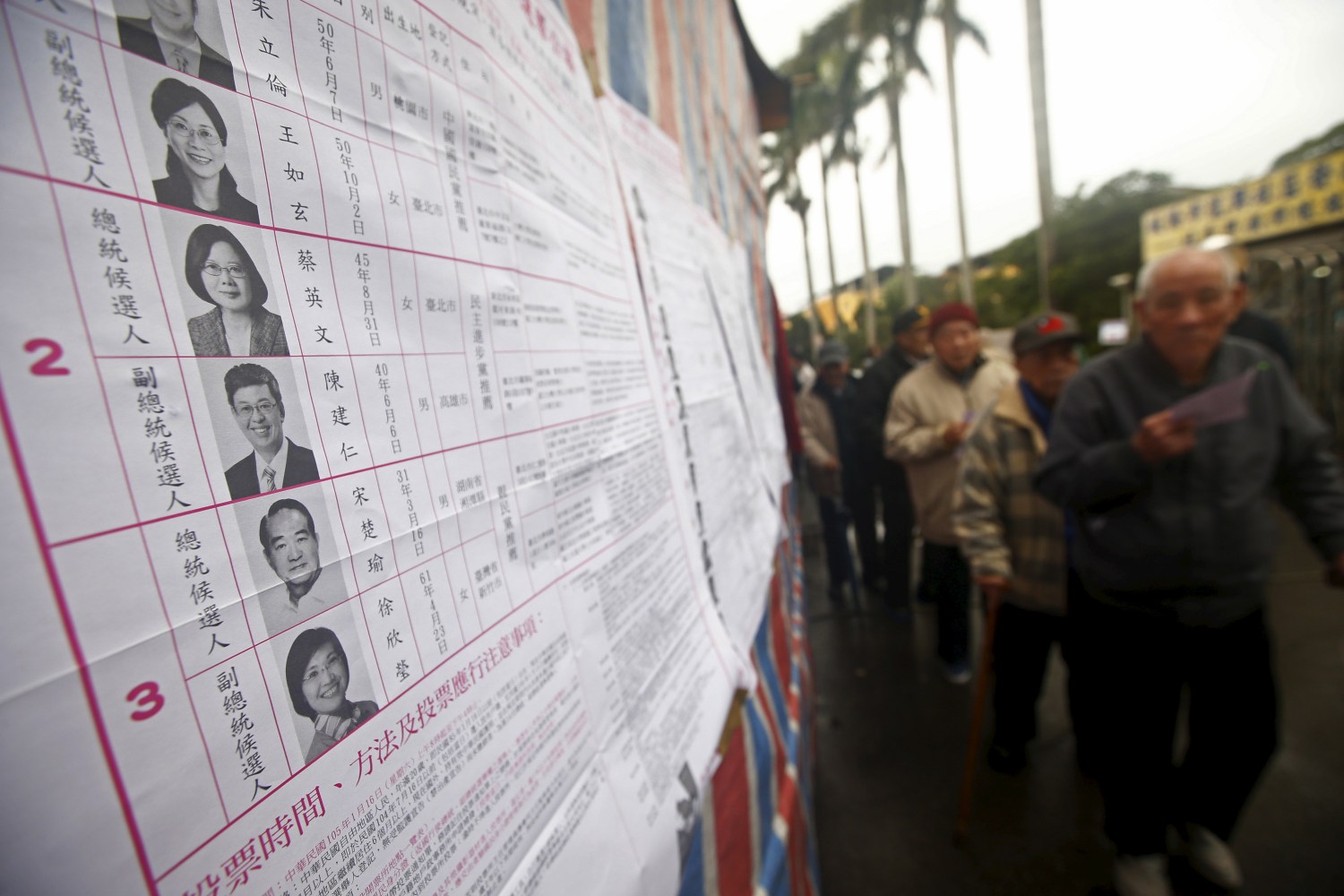 Voters queue next to a poster of candidates to cast their ballots at a polling station during general elections