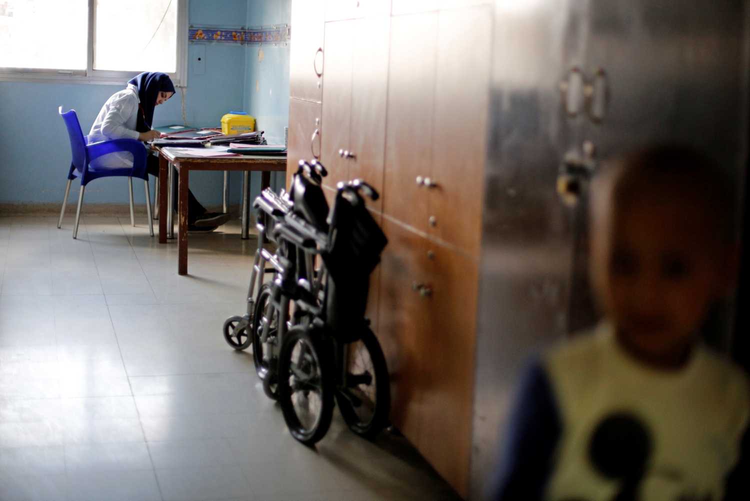 A young cancer patient stands as a nurse sits at a desk.