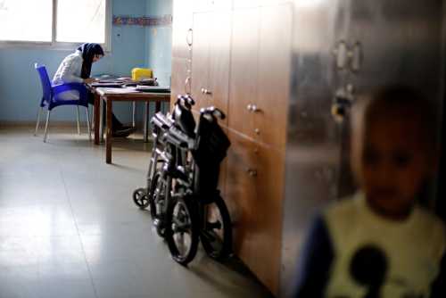 A young cancer patient stands as a nurse sits at a desk.