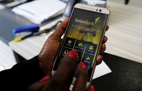 A customer uses her cell-phone to access the Sidian Bank mobile-app inside the banking hall at the Sidian Bank headquarters on the outskirts of Kenya's capital Nairobi